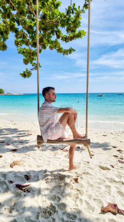 Photo for Men sitting on a swing at the beach of Koh Samet Island Rayong Thailand, the white tropical beach of Samed Island with a turqouse colored ocean - Royalty Free Image