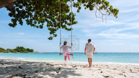 Photo for A couple of men and women at a swing on the beach of Koh Samet Island Rayong Thailand, the white tropical beach of Samed Island with a turqouse colored ocean. Asian woman and European men on vacation - Royalty Free Image
