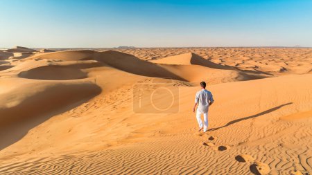 Photo for Dubai desert sand dunes, men on Dubai desert safari, United Arab Emirates vacation, men on vacation in Dubai Emirates walking in the sand dunes during vacation in Dubai - Royalty Free Image