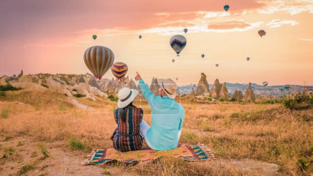 Téléchargez les photos : Cappadoce Turquie au lever du soleil, un couple d'hommes et de femmes d'âge moyen en vacances dans les collines de Goreme Cappadoce Turquie, hommes et femmes à la recherche lever du soleil avec des montgolfières en Cappadoce vacances en Turquie - en image libre de droit