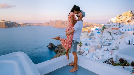 Photo for Santorini Greece, a young couple on luxury vacation at the Island Santorini watching the sunrise by the blue dome church and whitewashed village Oia Santorini during summer holidays - Royalty Free Image