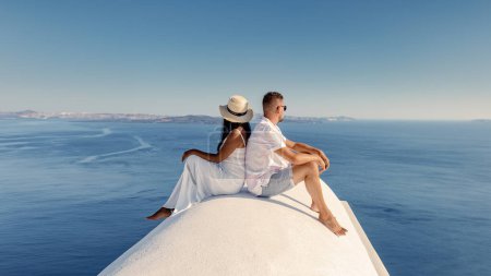 Foto de Santorini Grecia, una joven pareja de vacaciones de lujo en la Isla Santorini. hombres y mujeres sentados en una cúpula encalada junto al océano con vistas a la caldera de Santorini - Imagen libre de derechos