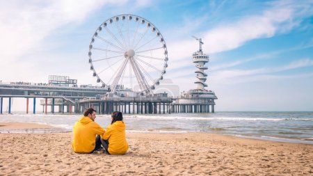 Téléchargez les photos : Couple sur la plage de Scheveningen Pays-Bas au printemps, La Grande Roue à la jetée à Scheveningen aux Pays-Bas, Ensoleillé jour de printemps à la plage - en image libre de droit