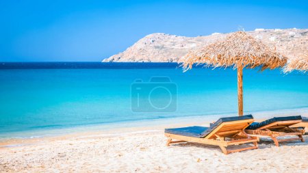 Téléchargez les photos : Mykonos plage en été avec parasol et chaises longues de luxe lits, océan bleu avec une montagne à la plage Elia Mikonos Grèce plage en été en Europe - en image libre de droit