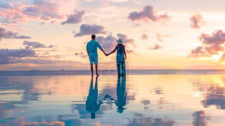 Photo for Young men and women watching the sunset with reflection in the infinity swimming pool at Saint Lucia Caribbean, a couple at infinity pool during sunset with a colorful sunset in the ocean - Royalty Free Image