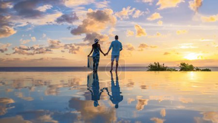 Foto de Young men and women watching the sunset with reflection in the infinity swimming pool at Saint Lucia Caribbean, couple at infinity pool during sunset - Imagen libre de derechos