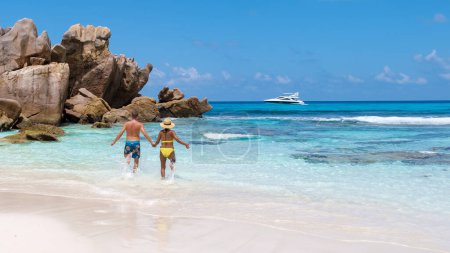 Téléchargez les photos : Anse Cocos Beach La Digue Island Seychelles, un couple heureux d'hommes et de femmes marchant sur la plage lors de vacances de luxe aux Seychelles, hommes et femmes sautant dans le ciel bonheur en vacances - en image libre de droit