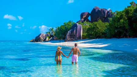 Téléchargez les photos : Anse Source d'Argent plage La Digue Island Seychelles, un couple d'hommes et de femmes marchant sur la plage lors de vacances de luxe. un couple nageant dans l'océan de couleur turqouse - en image libre de droit