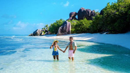 Foto de Anse Source d 'Argent beach La Digue Island Seychelles, un par de hombres y mujeres caminando por la playa en unas vacaciones de lujo. una pareja nadando en el océano de color turquesa de La Digue - Imagen libre de derechos