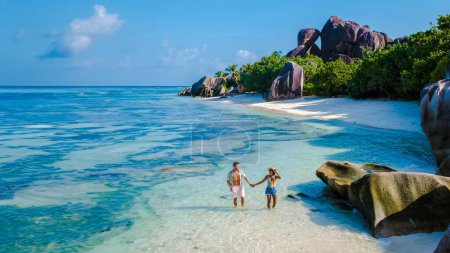 Téléchargez les photos : Anse Source d'Argent plage La Digue Island Seychelles, un couple d'hommes et de femmes marchant sur la plage lors de vacances de luxe. - en image libre de droit
