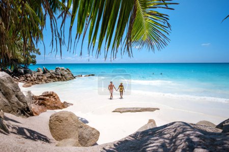 Téléchargez les photos : Anse Source d'Argent plage La Digue Island Seychelles, un couple d'hommes et de femmes marchant sur la plage lors de vacances de luxe. un couple nageant dans l'océan coloré de la maison turque pendant les vacances d'été - en image libre de droit
