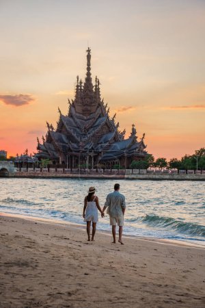 Téléchargez les photos : Un couple multiethnique diversifié d'hommes et de femmes visitent le temple en bois du Sanctuaire de la Vérité à Pattaya en Thaïlande. une construction de temple en bois situé au cap de Naklua Pattaya City Chonburi Thaïlande - en image libre de droit