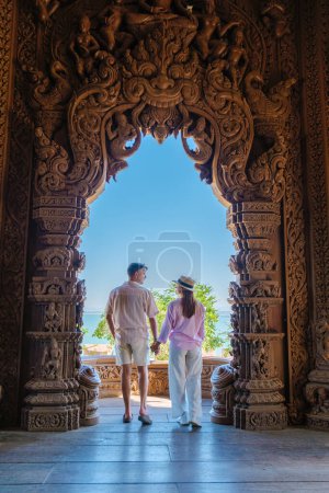 Téléchargez les photos : Un couple multiethnique diversifié d'hommes et de femmes visitent le temple en bois du Sanctuaire de la Vérité à Pattaya, Thaïlande, surplombant l'océan - en image libre de droit
