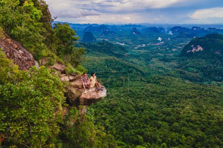 Foto de Dragon Crest Mountain Krabi Tailandia, una pareja joven se sienta en una roca que sobresale del abismo, con un hermoso paisaje. Cresta del Dragón o Khuan Sai en Khao Ngon Nak Nature Trail en Krabi, Tailandia - Imagen libre de derechos