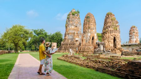 Téléchargez les photos : Ayutthaya Thaïlande à Wat Mahathat, un couple d'hommes et de femmes avec un chapeau et des cartes touristiques visitant Ayutthaya Thaïlande. Touristes avec une carte en est main regardant un temple en Thaïlande - en image libre de droit