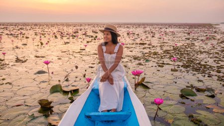Téléchargez les photos : La mer de lotus rouge, Lac Nong Harn, Udon Thani, Thaïlande. Femme asiatique avec un chapeau et une robe sur un bateau au lac Lotus rouge dans l'Isaan - en image libre de droit
