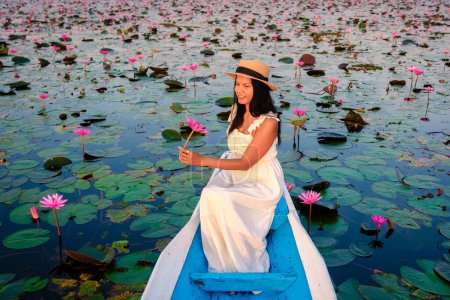 Téléchargez les photos : La mer de lotus rouge, Lac Nong Harn, Udon Thani, Thaïlande. Femme asiatique avec un chapeau et une robe sur un bateau au lac Lotus rouge dans l'Isaan - en image libre de droit