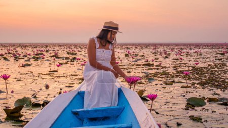 Foto de El mar de loto rojo, Lago Nong Harn, Udon Thani, Tailandia. Mujer asiática con sombrero y vestido en un barco en el lago de loto rojo en el Isaan al amanecer - Imagen libre de derechos