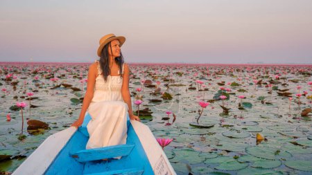 Téléchargez les photos : La mer de lotus rouge, Lac Nong Harn, Udon Thani, Thaïlande. Asiatique femme thaïlandaise avec un chapeau et une robe sur un bateau au lac Lotus rouge dans l'Isaan - en image libre de droit