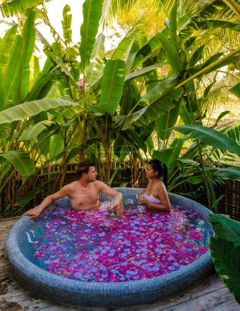 Téléchargez les photos : Un couple d'hommes et de femmes dans une baignoire extérieure dans un jardin verdoyant avec des feuilles, un couple d'hommes et de femmes dans une baignoire avec des fleurs au coucher du soleil dans une salle de bain extérieure - en image libre de droit