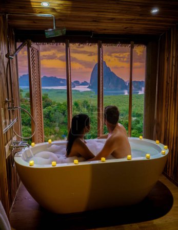 Photo for A couple of men and woman in a bathtub looking at the sunset over Sametnangshe viewpoint mountains in Phangnga Bay with mangrove forest in the Andaman Sea in Phangnga, Thailand, a couple in bathtub - Royalty Free Image