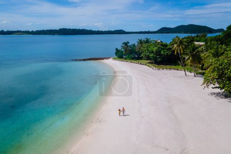 couple walking at the beach of Koh Kham Trat Thailand, aerial view of the tropical island near Koh Mak Thailand. white sandy beach with palm trees and big black boulder stones in the ocean