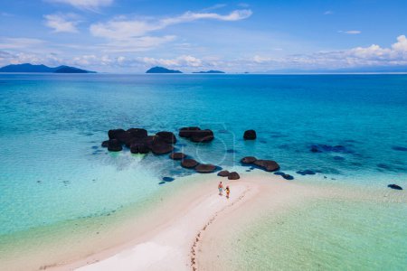 Foto de Pareja caminando en la playa de Koh Kham Trat Tailandia, vista aérea de la isla tropical cerca de Koh Mak Tailandia. playa de arena blanca con palmeras y grandes piedras de roca negra en el océano de Koh Kham - Imagen libre de derechos
