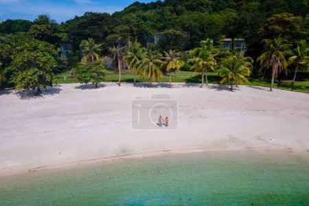 Foto de Pareja caminando en la playa de Koh Kham Trat Tailandia, vista aérea de la isla tropical cerca de Koh Mak Tailandia con una playa de arena blanca con palmeras y grandes piedras de roca negra en el océano - Imagen libre de derechos