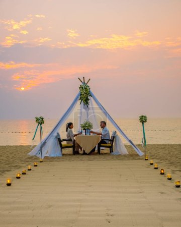 Foto de Cena romántica en la playa de Pattaya Tailandia, una pareja de hombres y mujeres de mediana edad cenando en la playa de Tailandia al atardecer con velas en la playa - Imagen libre de derechos