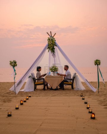 Foto de Cena romántica en la playa de Pattaya Tailandia, una pareja de hombres y mujeres de mediana edad cenando en la playa de Tailandia al atardecer con velas en la playa - Imagen libre de derechos