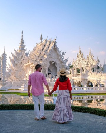 Foto de Templo Blanco Chiang Rai Tailandia, una diversa pareja de hombres europeos y mujeres asiáticas visitan el templo de Wat Rong Khun, al norte de Tailandia. - Imagen libre de derechos
