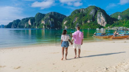 Foto de Un par de hombres y mujeres en Kho Phi Phi Tailandia caminando en la playa por la mañana, mañana soleada en Koh Phi Phi isla tropical en Tailandia con barcos de cola larga - Imagen libre de derechos