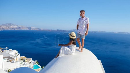 Foto de Una pareja viendo la puesta de sol en la cima de una cúpula de un hotel blanco de vacaciones en Santorini Grecia, Diversa pareja multirracial en las vacaciones de verano en Europa - Imagen libre de derechos