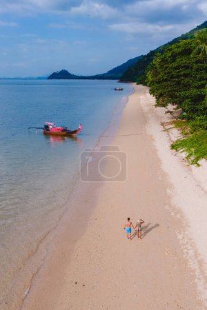 Téléchargez les photos : Une belle vue sur une plage calme avec une eau cristalline sur le ciel bleu à Koh Libong, province de Trang, Thaïlande, mer d'Andaman. Deux hommes et une femme marchant sur la plage par une soirée ensoleillée - en image libre de droit
