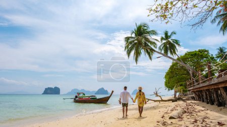 Téléchargez les photos : Un couple d'hommes européens et une femme asiatique thaïlandaise marchant sur la plage de l'île tropicale Koh Ngai Trang Thaïlande - en image libre de droit