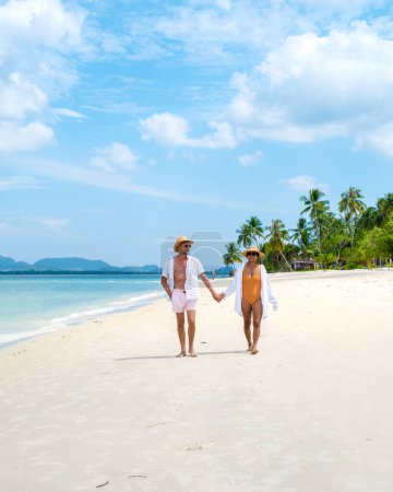 Photo for A young couple of caucasian men and a Thai Asian woman walking at the beach o Koh Muk a tropical island, with palm trees soft white sand, and a turqouse colored ocean, Koh Mook Trang Thailand - Royalty Free Image