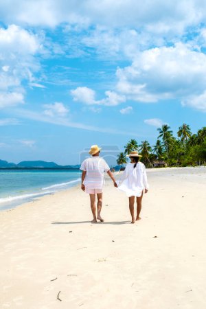 Foto de Una joven pareja de hombres caucásicos y una mujer asiática tailandesa caminando en la playa o Koh Muk una isla tropical, con palmeras de suave arena blanca, y un océano de color turquesa, Koh Mook Trang Tailandia - Imagen libre de derechos