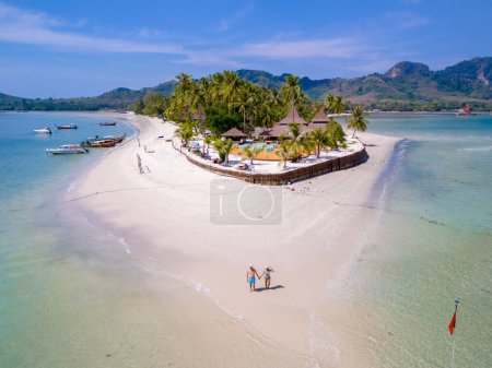 Photo for A couple of men and woman walking at the beach during a tropical vacation in Thailand, Koh Muk a tropical island with palm trees soft white sand, and a turqouse colored ocean in Thailand - Royalty Free Image