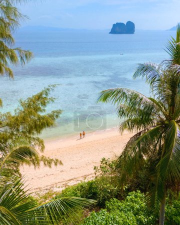 Téléchargez les photos : Vue entre les feuilles de palmier à un couple d'hommes et de femmes sur la plage de l'île de Koh Ngai en Thaïlande, avec des palmiers et du sable blanc doux, et une turque couleur océan à Koh Ngai Trang Thaïlande - en image libre de droit