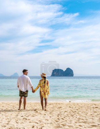 Foto de Feliz pareja joven, una mujer asiática y un hombre europeo en la playa de la isla de Koh Ngai, arena blanca y suave, y un océano de color turquesa en Koh Ngai Trang Tailandia - Imagen libre de derechos