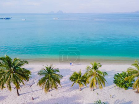 Photo for Drone view at a couple walking on the white sandy tropical beach of Koh Muk with palm trees soft white sand, and a turqouse colored ocean in the evening in Koh Mook Trang Thailand - Royalty Free Image