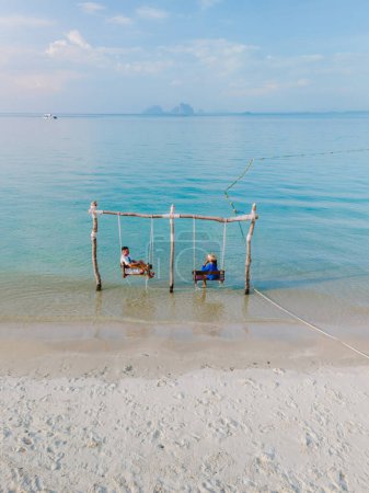 Téléchargez les photos : Un couple d'hommes et une femme sur une balançoire à la plage de Koh Muk île tropicale, et une turque couleur océan à Koh Mook Trang Thaïlande, un couple sur une balançoire dans l'océan - en image libre de droit