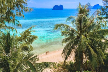 Foto de Vista entre hojas de palmera en una pareja en la playa, vista aérea de Drone en la isla de Koh Ngai con palmeras y arena blanca suave, y un océano de color turquesa en Koh Ngai Trang Tailandia - Imagen libre de derechos