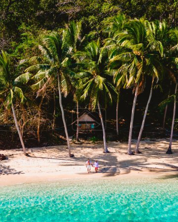Foto de Vista superior de una pareja en una playa tropical con al fondo un pequeño bungalow de madera, océano de color turquesa con palmeras, hombre y mujer de pie junto al océano durante las vacaciones en Tailandia - Imagen libre de derechos