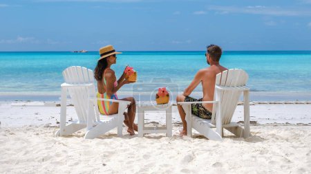 Téléchargez les photos : Couple hommes et femmes sur la plage avec une boisson à la noix de coco à Praslin Island Seychelles, couple en vacances de luxe relaxant au bord de l'eau, homme et femme en vacances tropicales - en image libre de droit