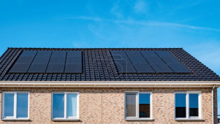 Téléchargez les photos : Maisons nouvellement construites avec des panneaux solaires noirs sur le toit contre un ciel ensoleillé, Gros plan du nouveau bâtiment avec des panneaux solaires noirs par une journée ensoleillée - en image libre de droit