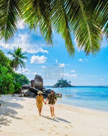 Téléchargez les photos : Homme et femme en vacances aux Seychelles Mahe, une plage tropicale avec des palmiers et un océan bleu Anse Royale Beach, un couple diversifié de femmes asiatiques et d'hommes caucasiens marchant main dans la main sur la plage - en image libre de droit