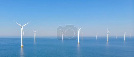 Foto de Un parque eólico con hileras de turbinas eólicas en medio del océano, mezclándose con el paisaje natural entre el agua y el cielo azul - Imagen libre de derechos