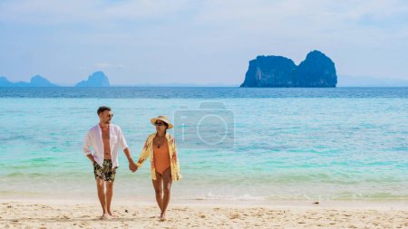 Téléchargez les photos : Heureux jeune couple, une femme asiatique et un homme européen sur la plage de l'île de Koh Ngai, sable blanc doux, et un océan de couleur turque par une journée ensoleillée, homme en maillot de bain court et blanc, femme en bikini - en image libre de droit