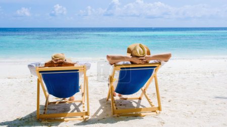 Foto de Vista trasera de un par de hombres y mujeres sentados relajándose en sillas de playa en Koh Lipe Island Sur de Tailandia, turqouse color océano y playa de arena blanca, diversa pareja luna de miel o concepto de vacaciones - Imagen libre de derechos